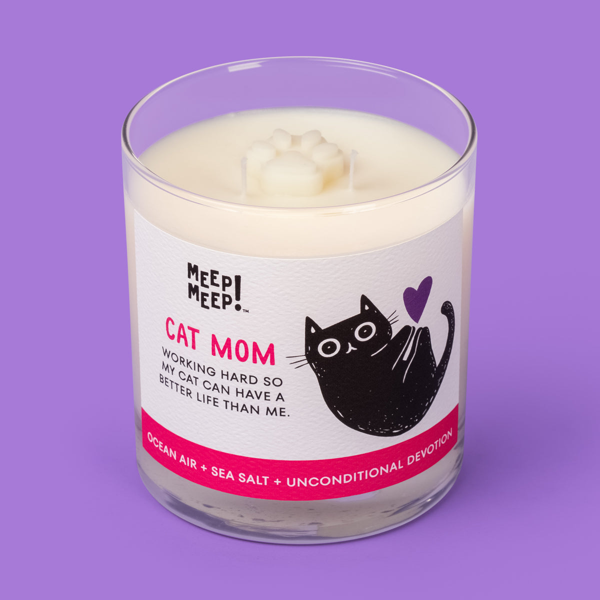 Meep Meep Cat Mom candle in a clear glass jar with a white and pink label featuring a curled black cat and purple heart. Jar is angled so we can see the paw embed on top of candle.