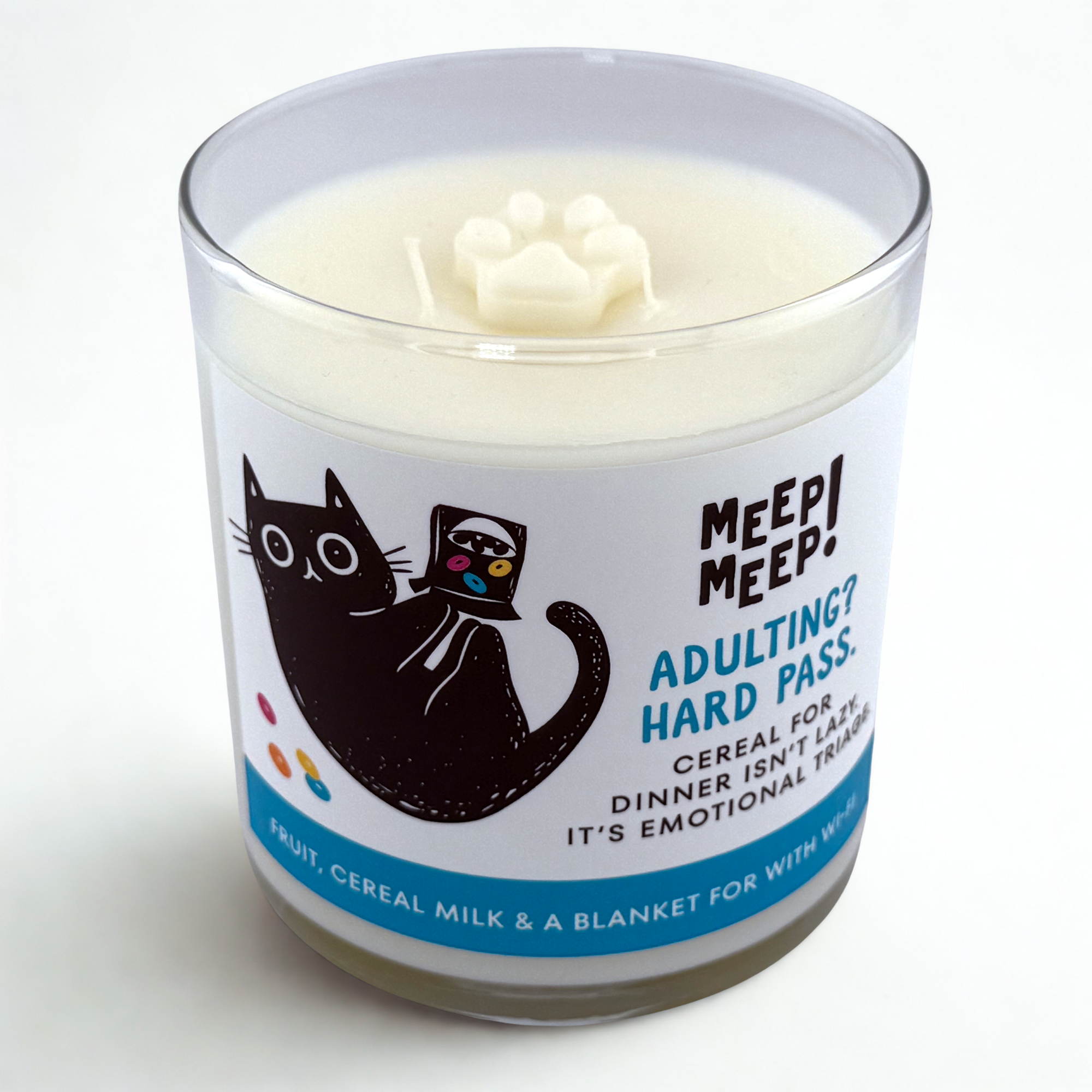 Photograph of Meep Meep candle with wax paw print embed on top. Label has an Illustration of a black cat on it's back playing with a box of cereal and some colored fruit loop-like cereal on the floor. Text on white background says "Adulting?Hard Pass. Cereal fordinner isn’t lazy. It’s emotional triage."
Bottom of candle label reads fruit, cereal milk & a blanket forT with wi-fi