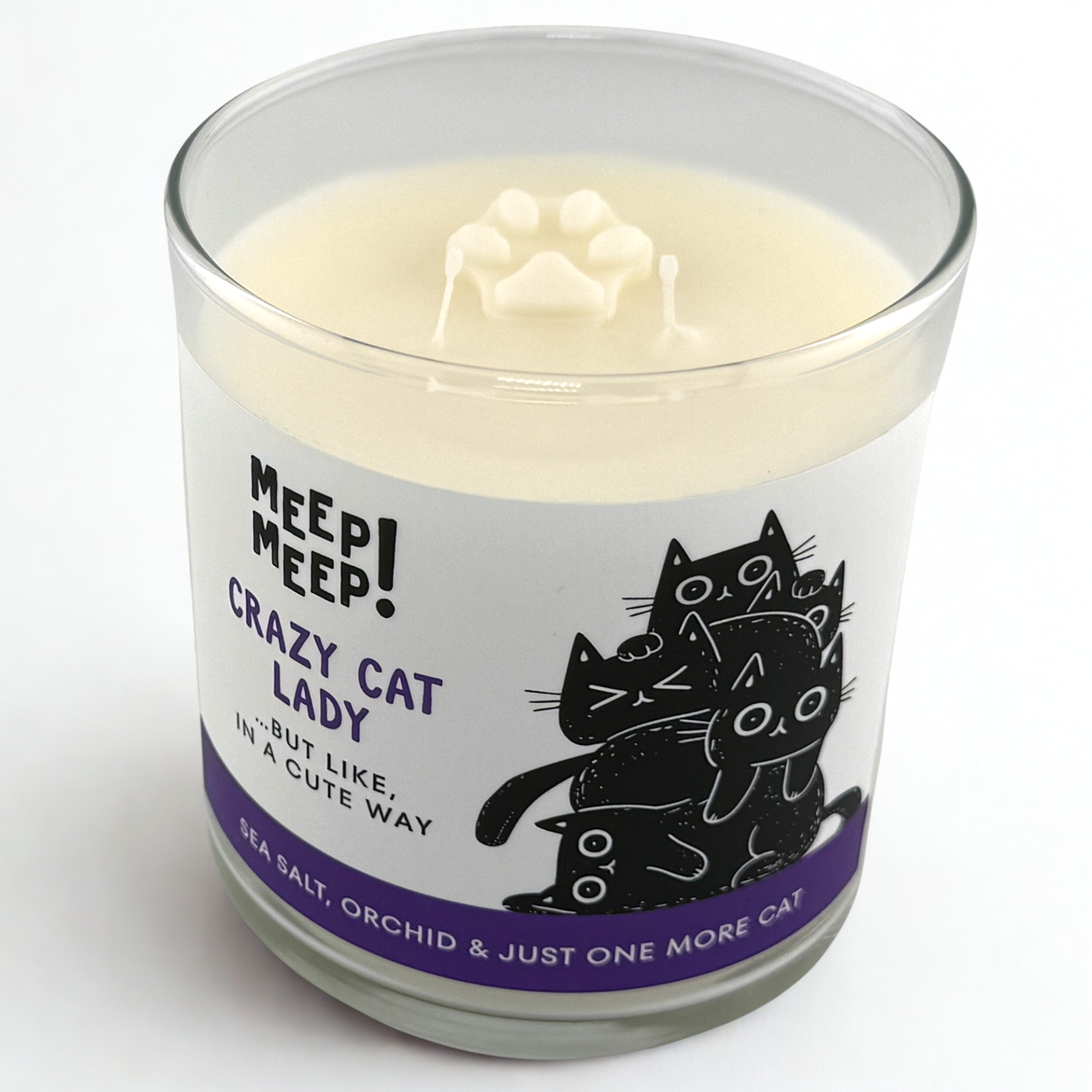 Photograph of Meep Meep candle with wax paw print embed on top. Label has an Illustration of a five black cats piled ontop of eachother. Text on white background says "Crazy CATLADY. …but like,
in a cute way"
Bottom of candle label reads Sea Salt, Orchid & just one more cat