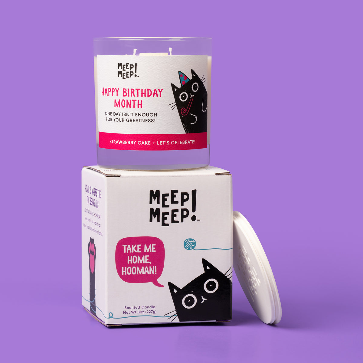 Happy Birthday Month candle on its cat-themed gift box reading “Take me home, hooman!” with a white lid beside it.