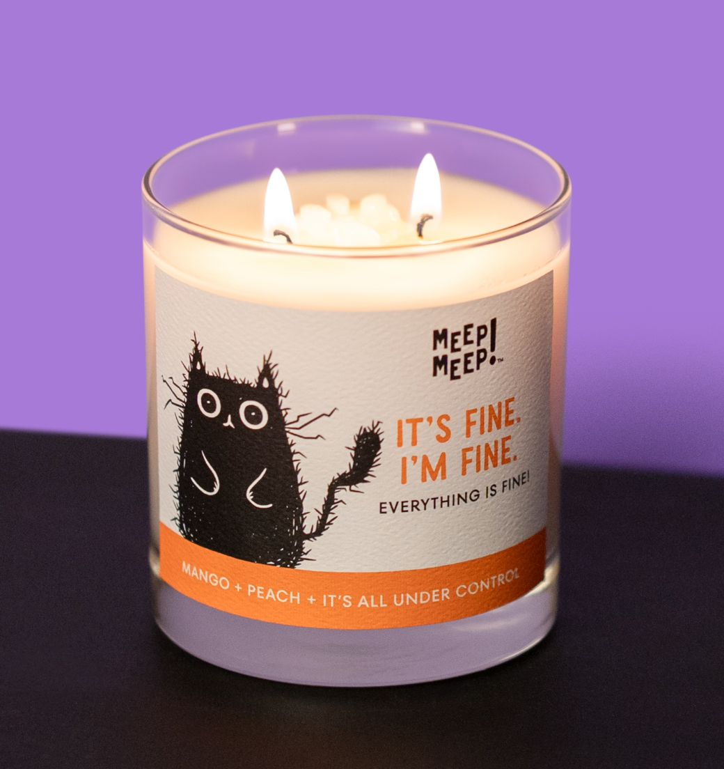 A Meep Meep double-wick candle in a clear glass jar with a white label featuring a black cat illustration and the text 'IT'S FINE. I'M FINE. EVerything is Fine!