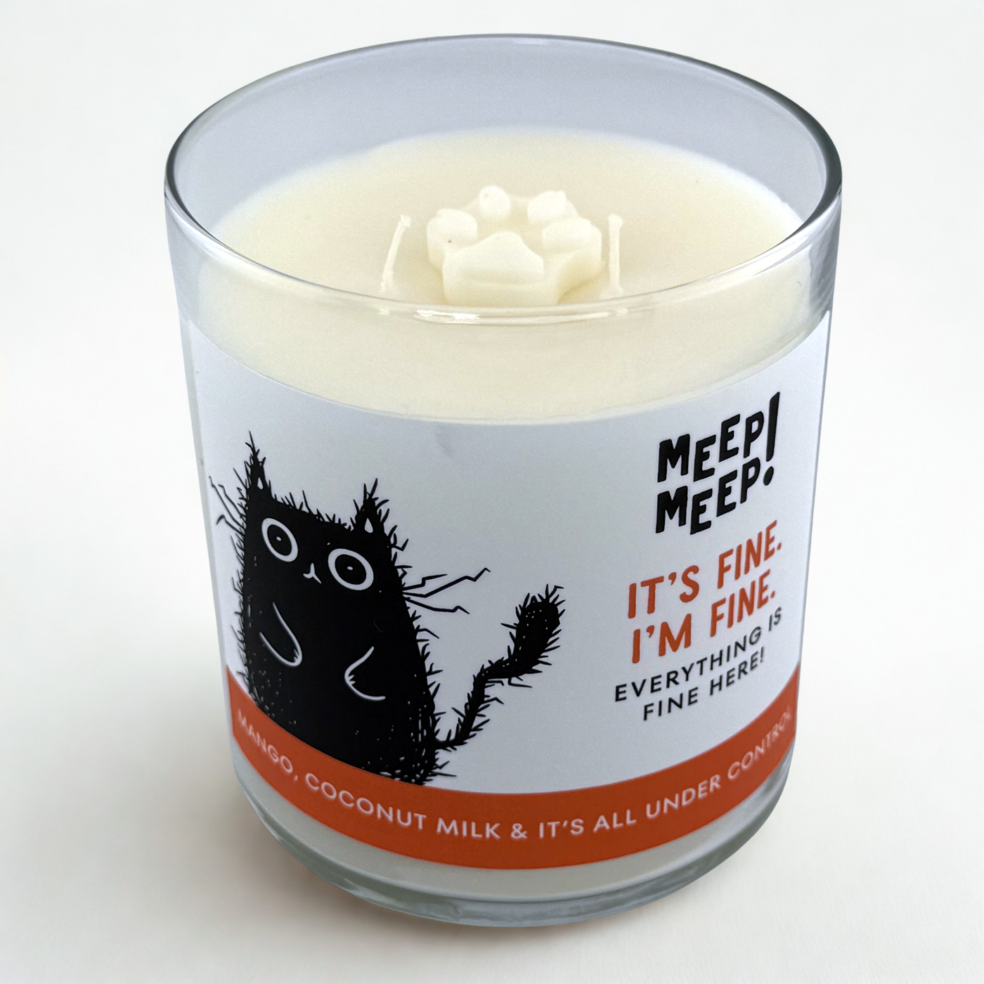 Photograph of Meep Meep candle with wax paw print embed on top. Label has an Illustration of a black cat who looks electrocuted. Text on white background says "it’s fine.i’m fine.  everything isfine here!"
Bottom of candle label reads mango, coconut milk & it’s all under control