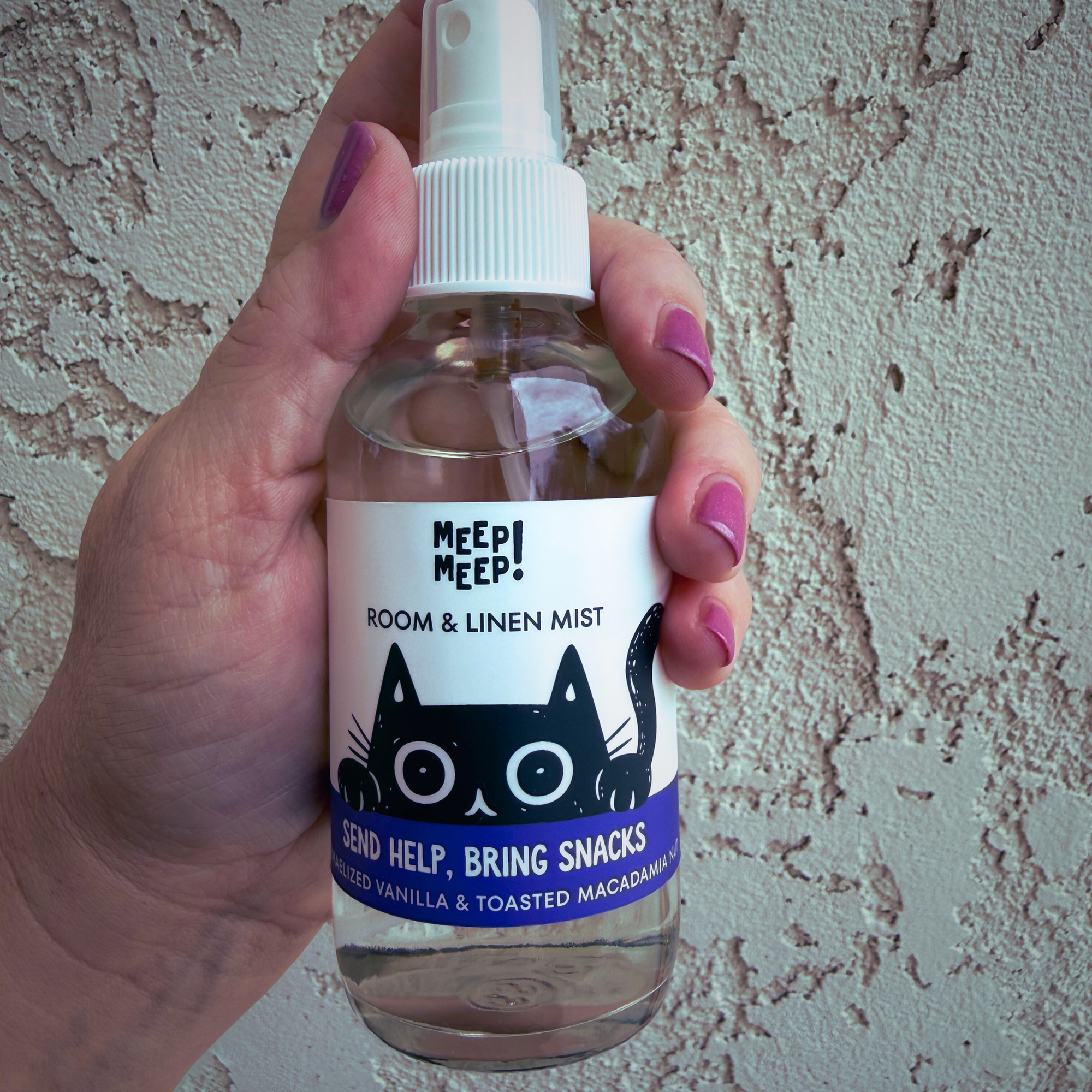 Image of glass bottle with illustration of black cat peeking out. Label on bottle reads: Meep Meep Odor-eliminating room & linen spray. "Send Help, Bring Snacks" , caramelized vanilla, toasted macadamia nut & a case of the Mondays.