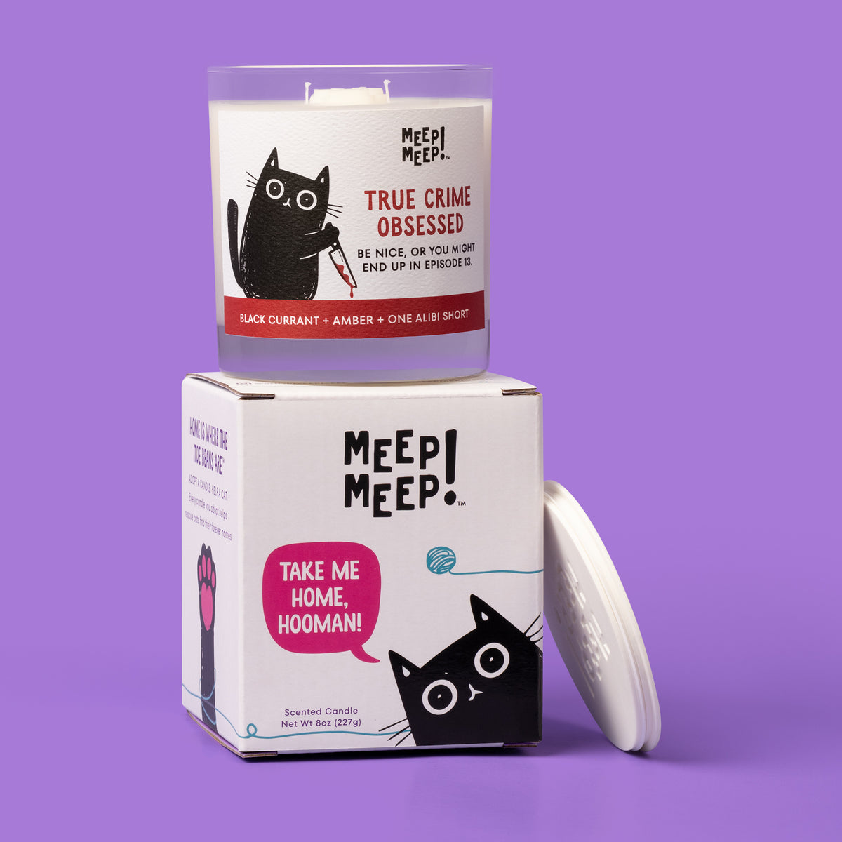 True Crime Obsessed candle on its cat-themed gift box reading “Take me home, hooman!” with a white lid beside it.