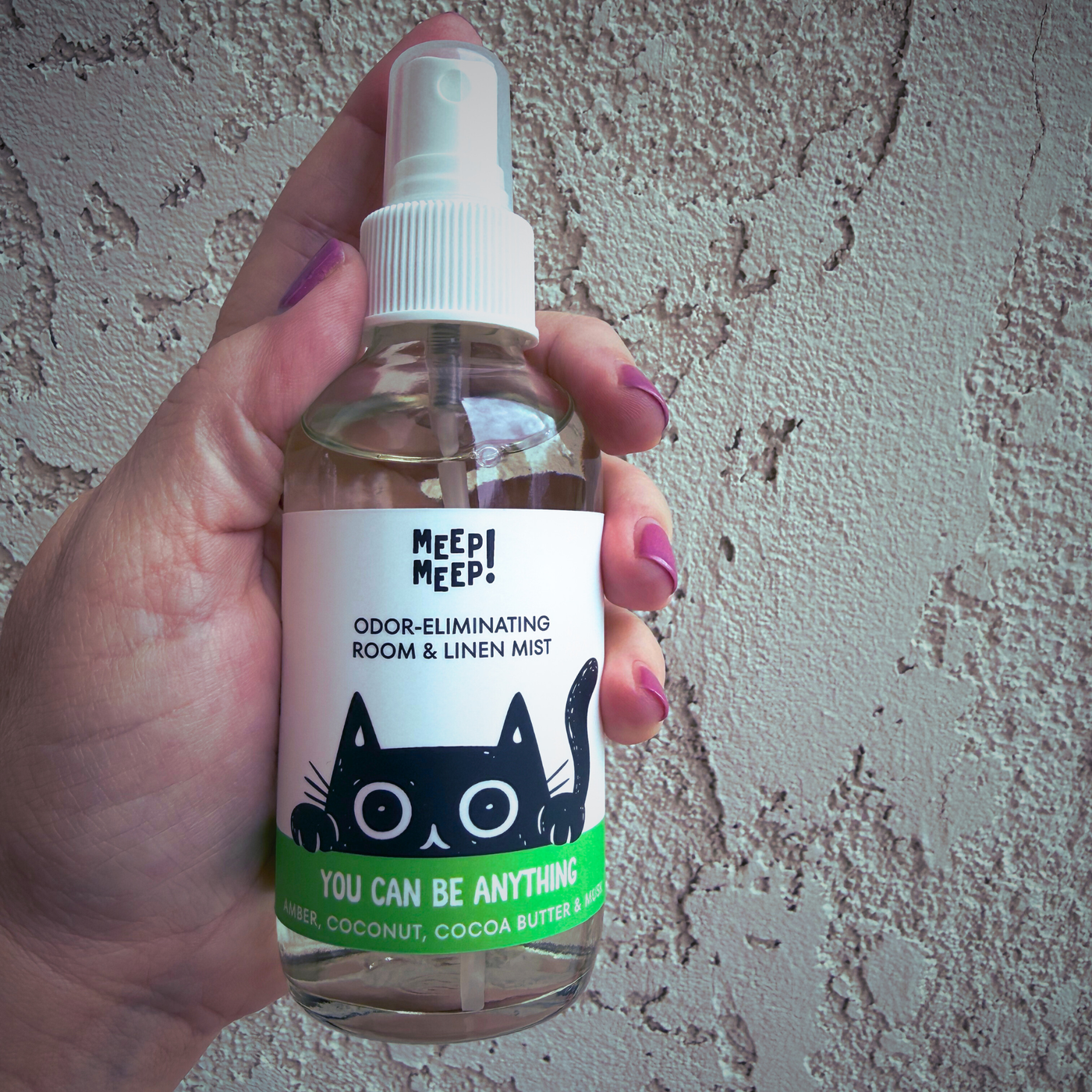 Image of glass bottle with illustration of black cat peeking out. Label on bottle reads: Meep Meep Odor-eliminating room & linen spray. "You Can Be Anything" , Amber, Coconut, Cocoa Butter & Musk