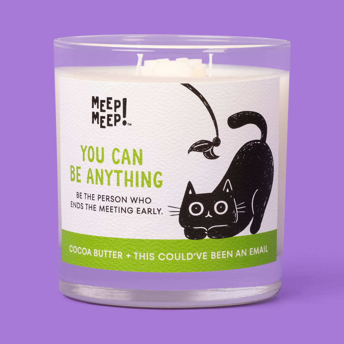 Meep Meep You Can Be Anything candle in a clear glass jar with a green label featuring a black cat crouching beneath a feather toy.