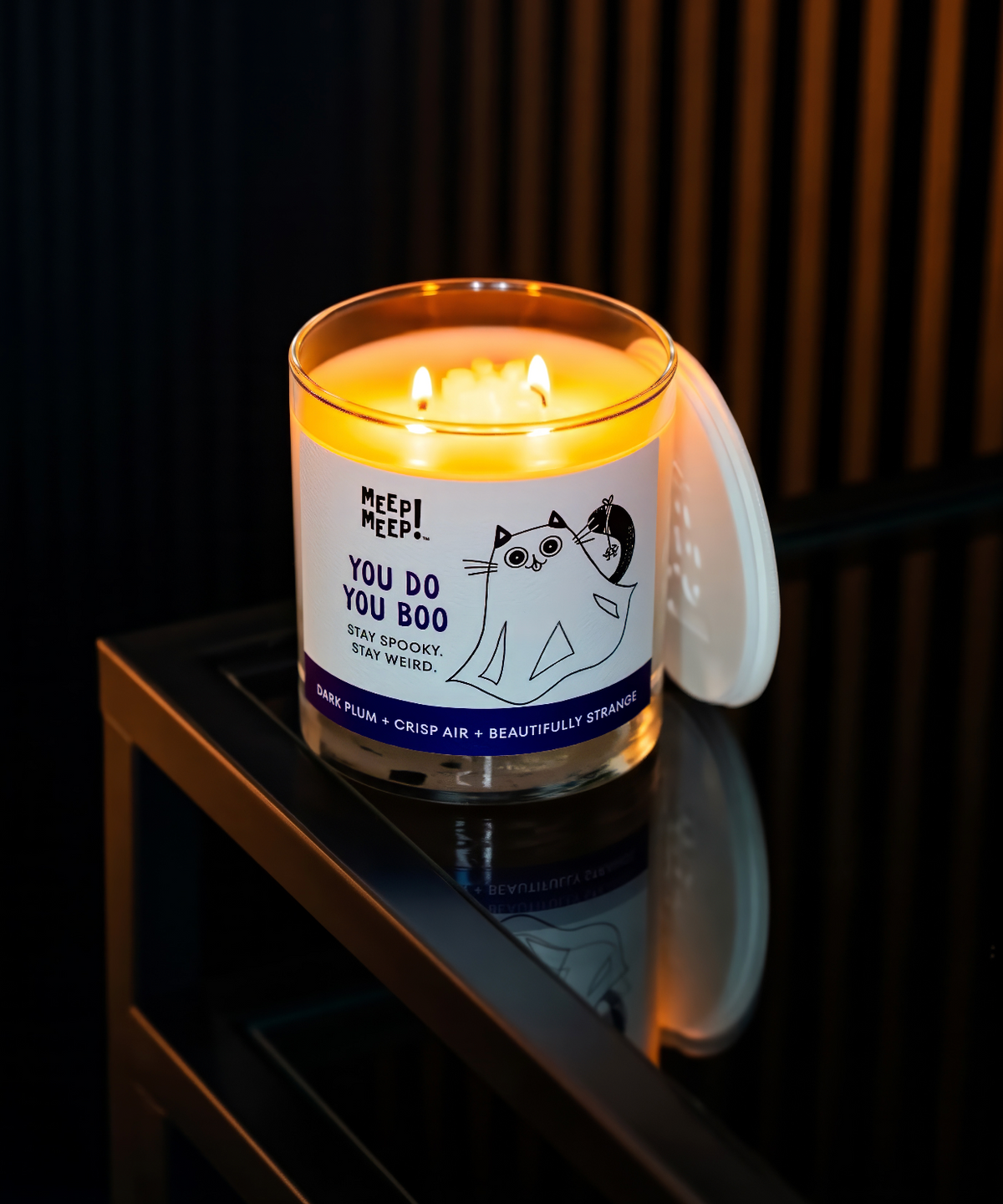 Photo of Meep Meep You Do You Boo candle lit sitting on dark table. Candle label has illustration of black cat dressed as a ghost. 